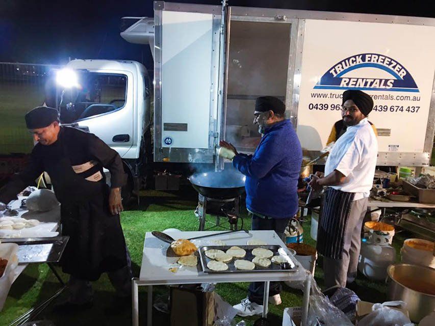 A group of men are preparing food in front of a truck that says truck freezer rentals