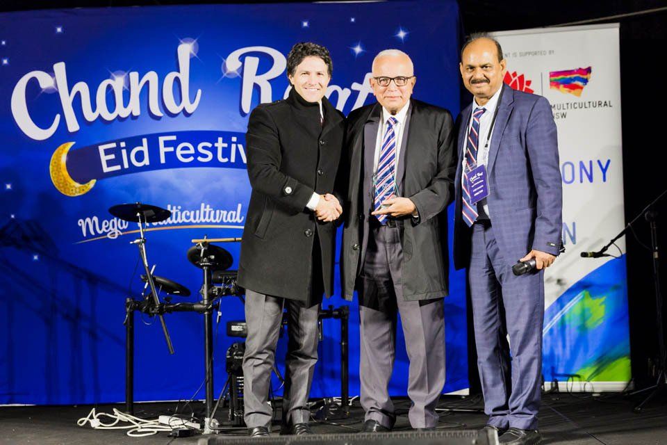Three men are standing next to each other in front of a stage.