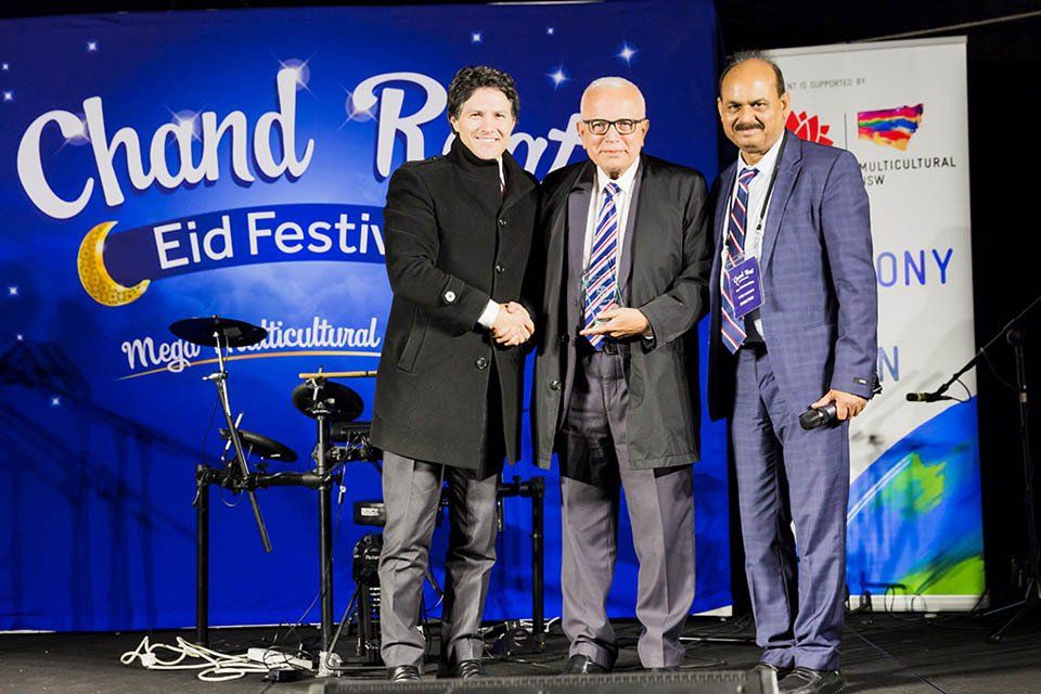 Three men are posing for a picture in front of a sign that says chand resort eid festival