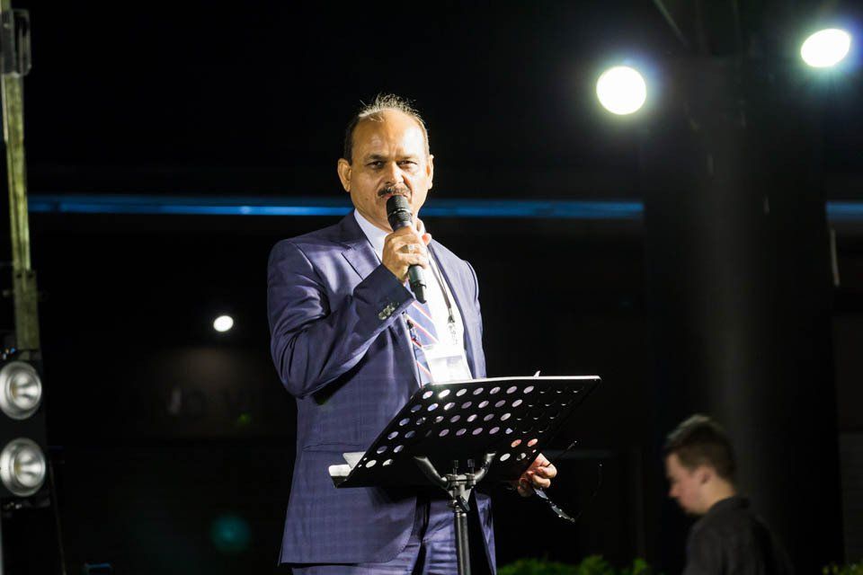 A man in a suit is standing at a podium holding a microphone.