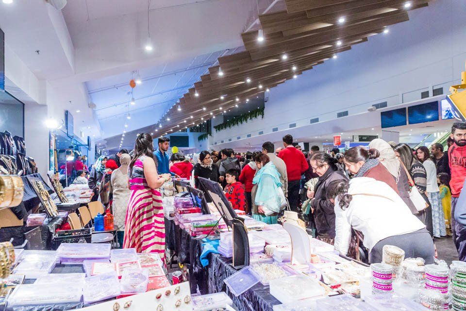 A crowd of people are standing around tables at a market.
