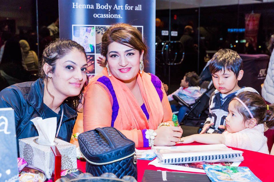 A group of people are sitting at a table with a sign that says henna body art for all occasions.