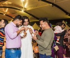 A group of men are eating food at a party while a woman holds a baby.