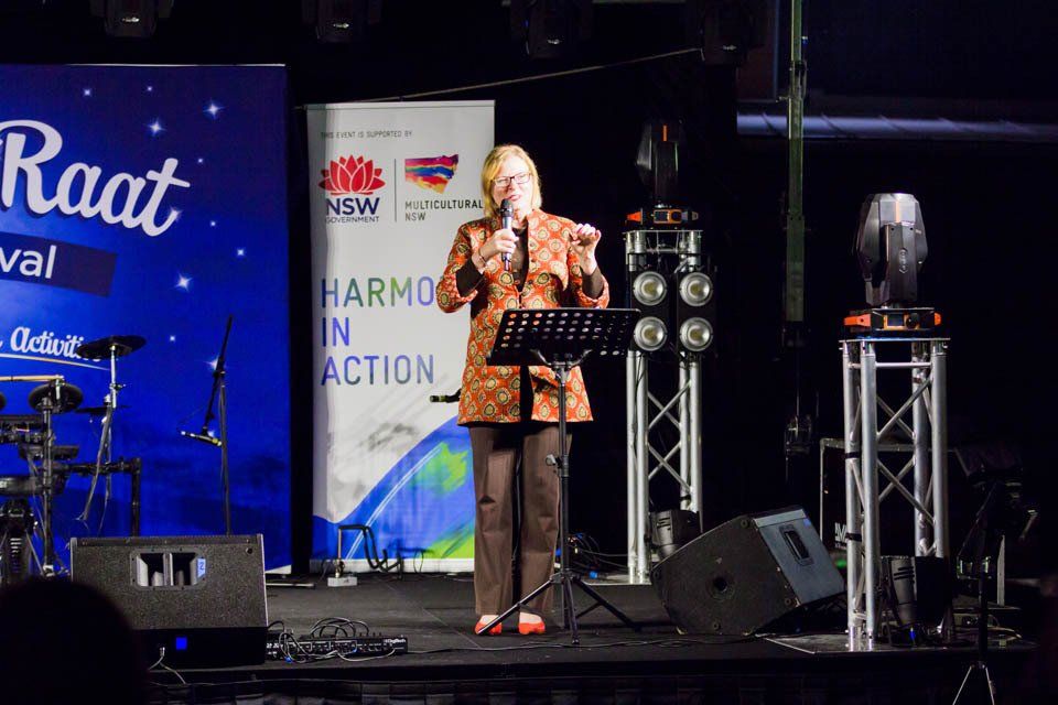 A woman singing into a microphone in front of a sign that says raat