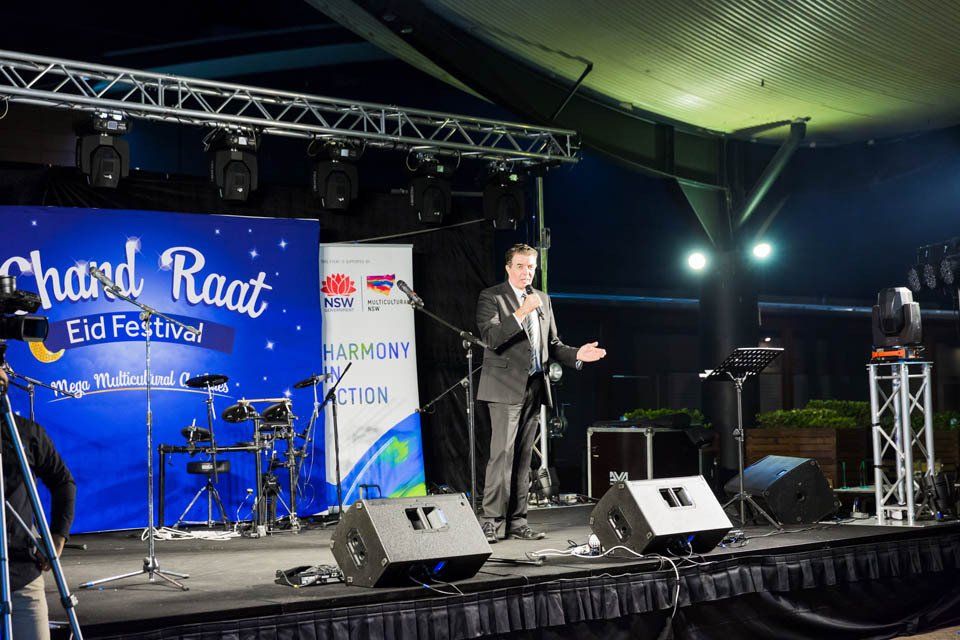 A man is standing on a stage in front of a sign that says chand raat