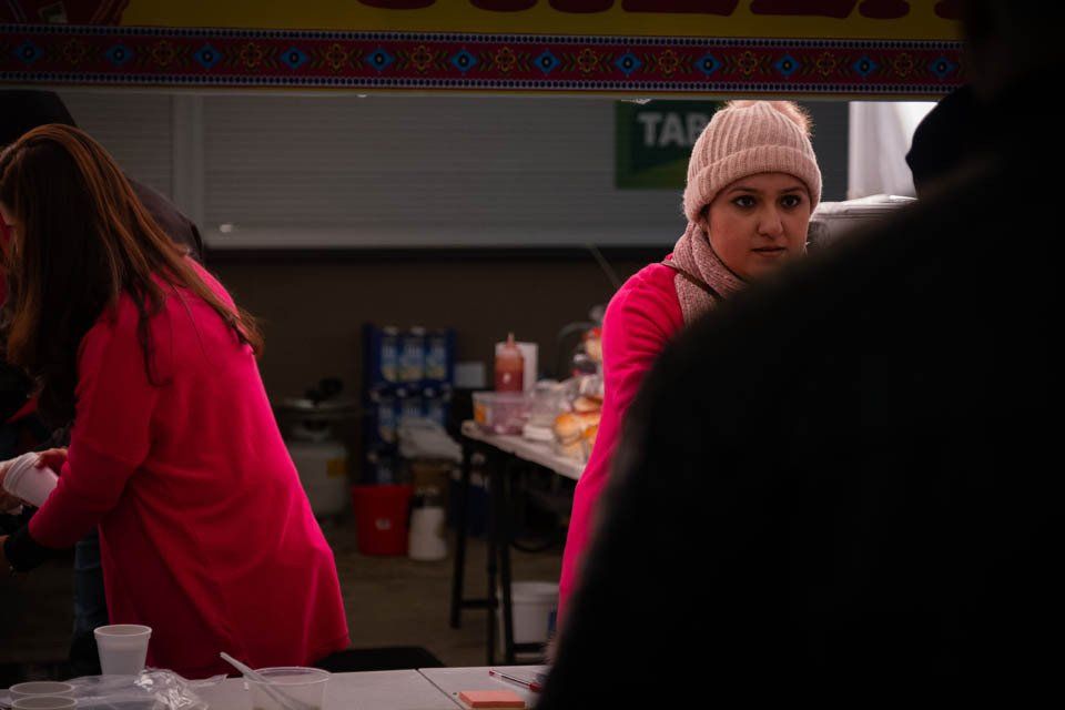 A woman in a pink dress and a pink hat is standing in front of a table.