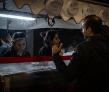 A man is talking on a cell phone while standing in front of a food stand.