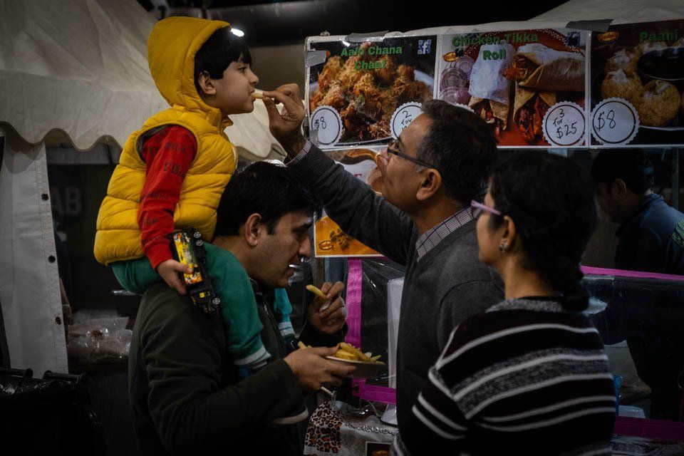 A man is feeding a child a piece of food at a food festival.