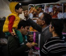 A man is carrying a child on his shoulders at a food festival.