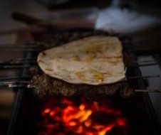 A piece of bread is sitting on top of a piece of meat on a grill.