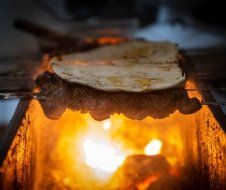 A tortilla is sitting on top of a piece of meat on a grill.