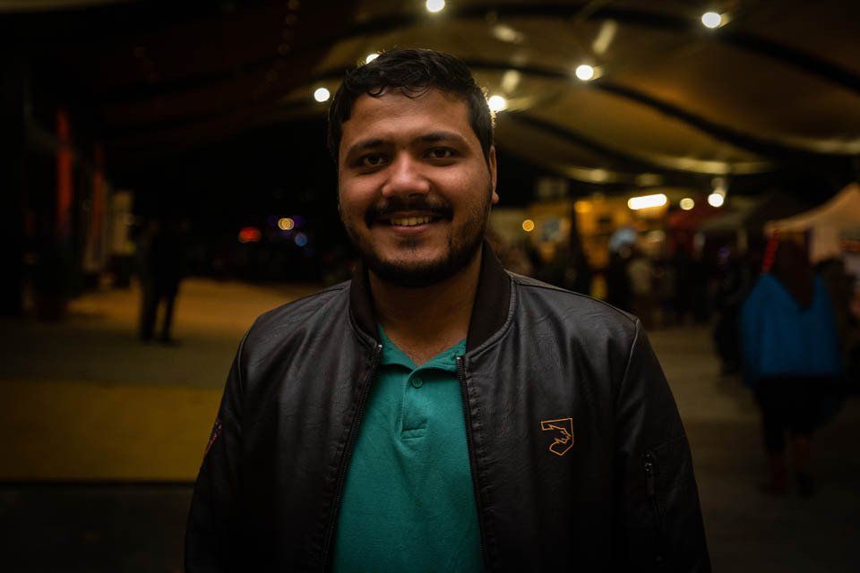 A man with a beard is wearing a leather jacket and a green shirt.