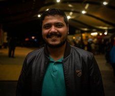 A man with a beard is wearing a leather jacket and a green shirt.