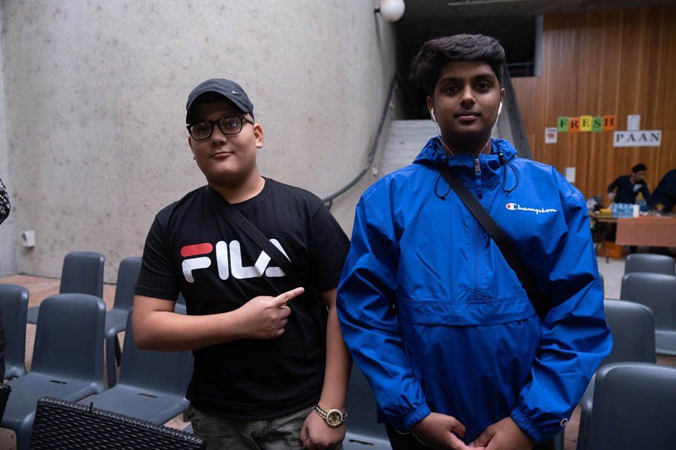 Two young men are standing next to each other in a room . one of the men is wearing a fila shirt.