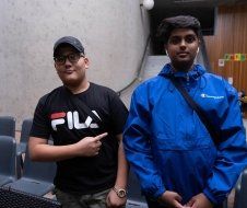 Two young men are standing next to each other in a room . one of the men is wearing a fila shirt.