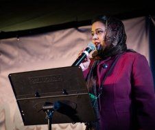 A woman is singing into a microphone while wearing a head scarf.