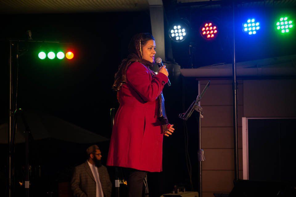 A woman in a red coat is standing on a stage holding a microphone.