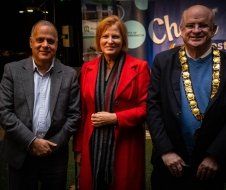 A woman in a red coat is standing between two men in suits.