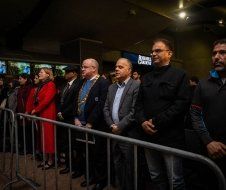 A group of people are standing behind a metal barrier.