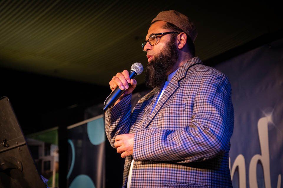 A man with a beard and glasses is holding a microphone on a stage.
