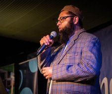 A man with a beard is standing in front of a microphone.