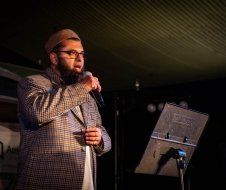A man with a beard is standing in front of a microphone on a stage.