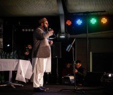 A man with a beard is standing on a stage holding a microphone.