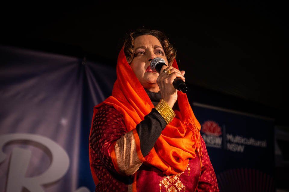 A woman in an orange scarf is singing into a microphone.
