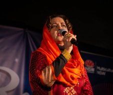 A woman in an orange scarf is singing into a microphone.