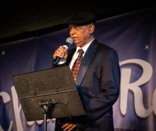 A man in a suit and tie is standing at a podium holding a microphone.