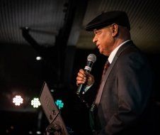 A man in a suit and hat is holding a microphone.
