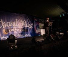 A man is standing on a stage in front of a large blue banner.