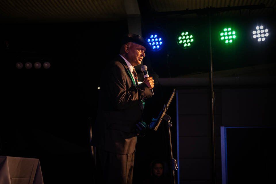 A man in a suit and tie is standing in front of a microphone in a dark room.