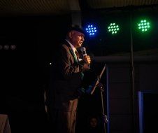 A man in a suit is standing in front of a microphone in a dark room.