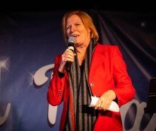 A woman in a red jacket is holding a microphone.