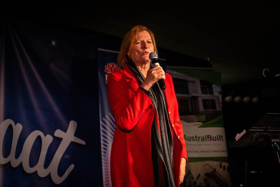 A woman in a red coat is standing in front of a microphone.