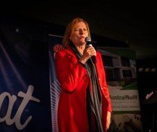 A woman in a red coat is singing into a microphone.