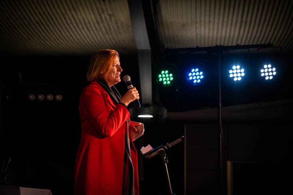 A woman in a red coat is standing in front of a microphone.