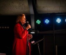 A woman in a red coat is standing in front of a microphone.
