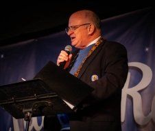 A man in a suit is standing at a podium holding a microphone.