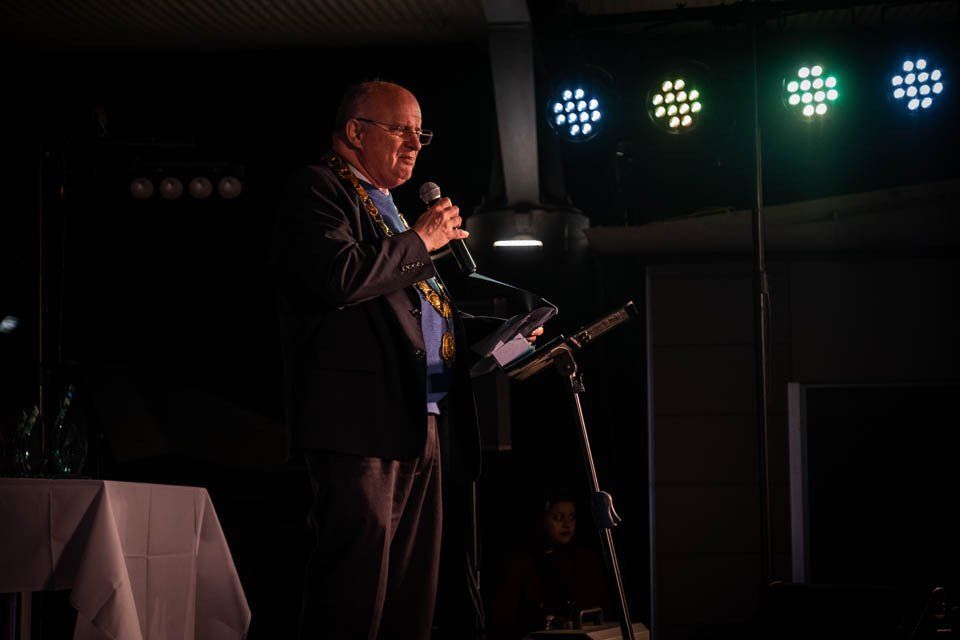 A man in a suit is standing at a podium holding a microphone.