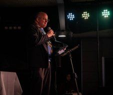 A man in a suit is standing at a podium holding a microphone.