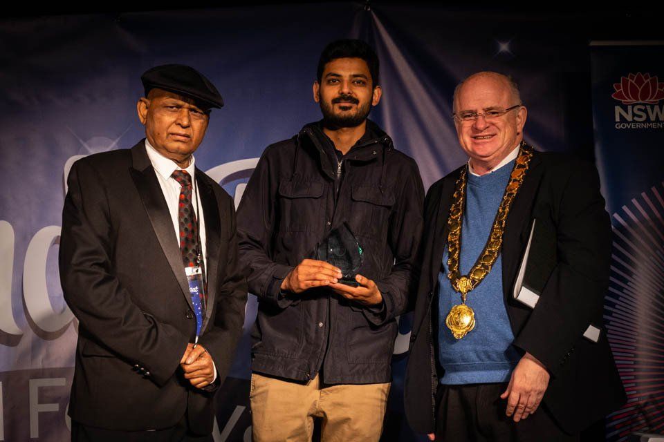 Three men are standing next to each other and one of them is holding an award.