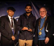 Three men are standing next to each other and one of them is holding a trophy.