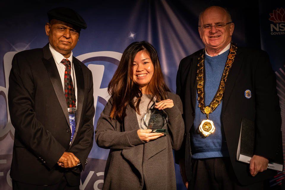 A woman is holding an award while standing between two men in suits.