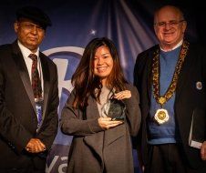 A woman is holding a trophy while standing next to two men in suits.