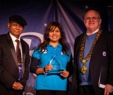 A woman in a blue shirt is standing between two men in suits.