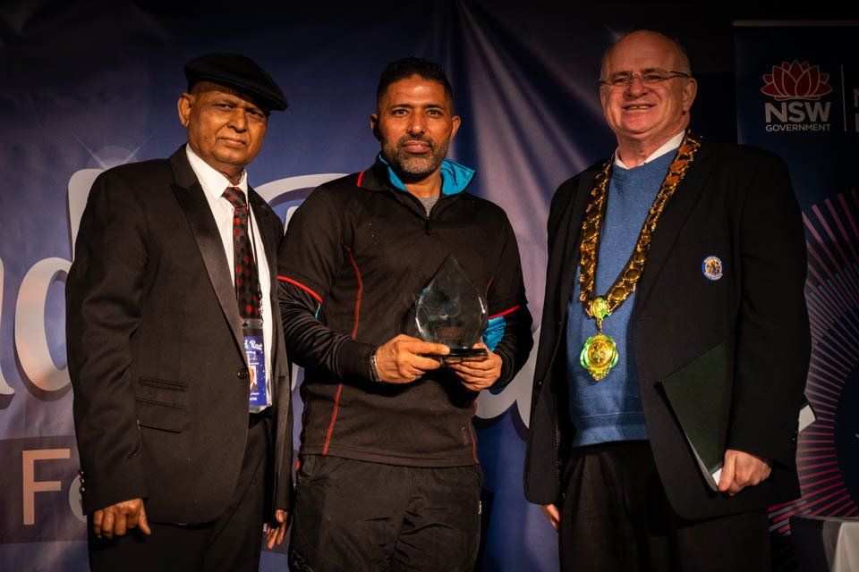 Three men are standing next to each other and one of them is holding an award.