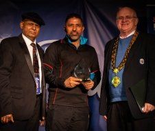 Three men are standing next to each other and one of them is holding a trophy.