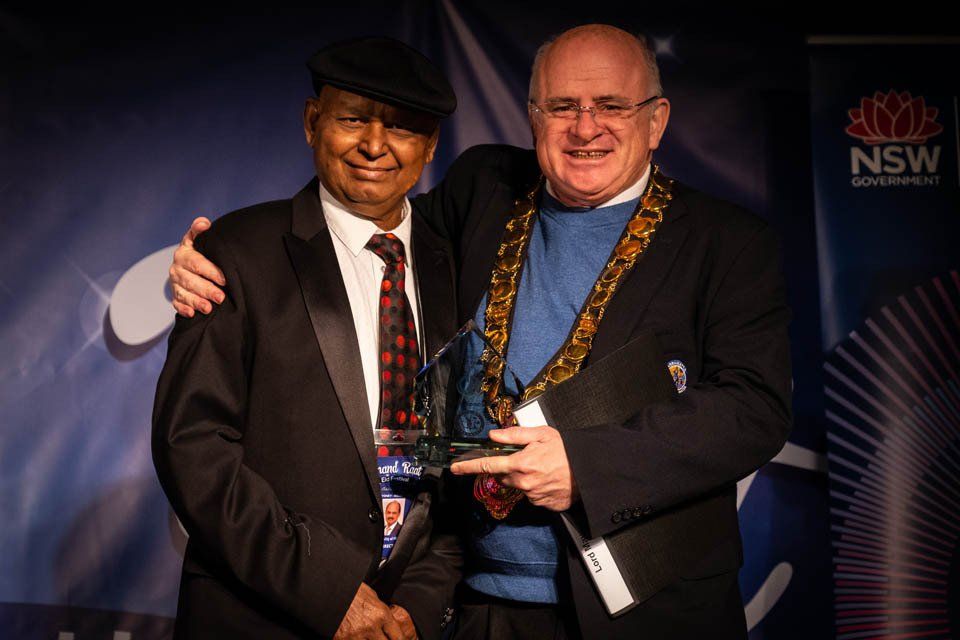 Two men are standing next to each other and one is holding a trophy.